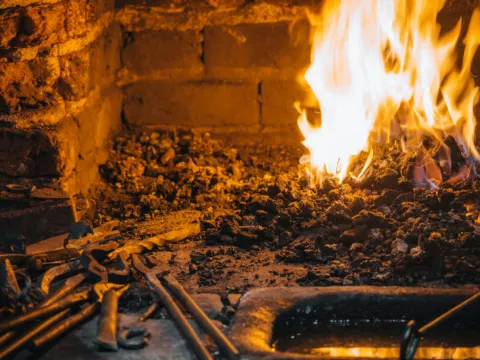 Foyer de forge en briques avec flammes, braises et outils de ferronnier posés devant