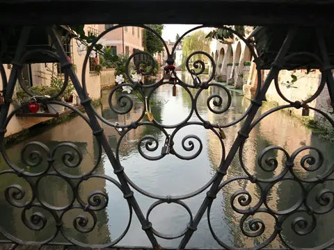Garde-corps de fer forgé à grandes volutes sur un pont, avec vue sur un canal bordé de maisons
