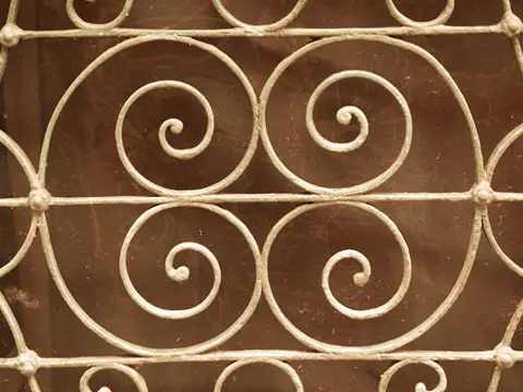 Détail d'une grille en fer forgé peinte en blanc cassé, à quatre grandes spirales reliées par des barres