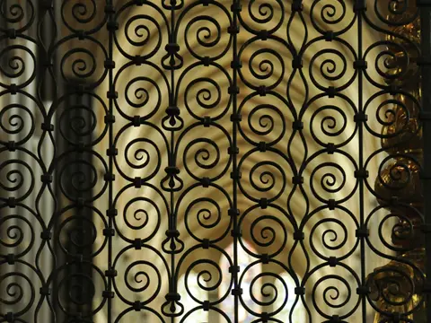Grille de fer forgé noir à motifs de volutes serrées, vue de près, devant une ouverture en arc éclairée