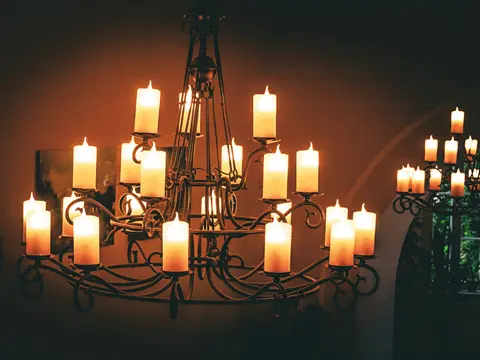 Grand lustre en fer forgé portant de nombreuses bougies allumées, dans une pièce sombre