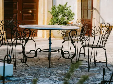 Table ronde et chaises en fer forgé à dossiers ajourés sur une terrasse en pierre, devant une porte en bois