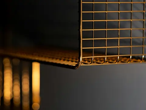 Gros plan sur une étagère en grillage d'acier doré à angles arrondis, éclairée par une lumière chaude, fond sombre et lumières floues