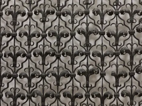 Panneau de fer forgé noir ajouré, fait de fleurs de lys et d'acanthes entrelacées, sur un fond clair, vu de face en lumière douce