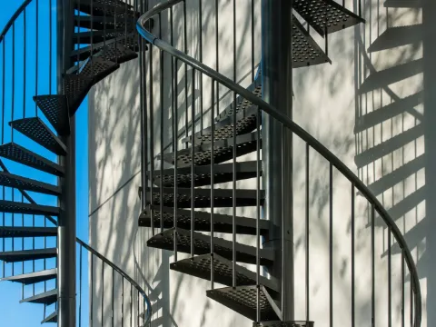 Escalier colimaçon extérieur à marches ajourées en acier noir devant un mur clair