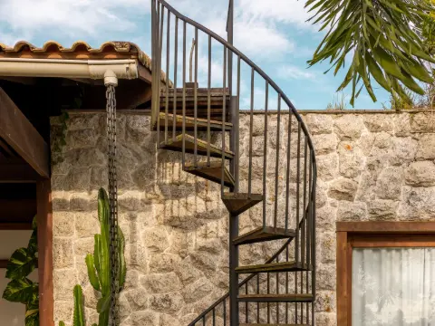 Colimaçon en acier noir contre un mur de pierre dans une cour de villa plantée