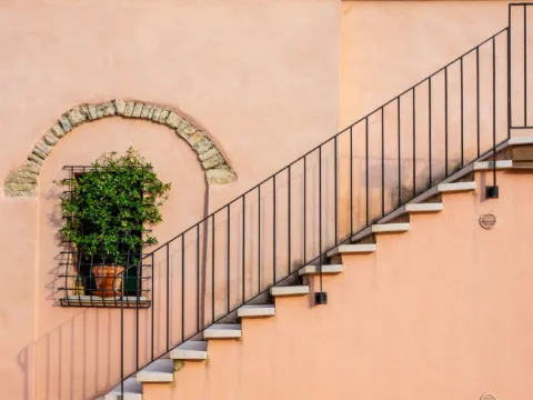 Escalier extérieur longeant un mur ocre rosé, avec fine rampe en fer noir