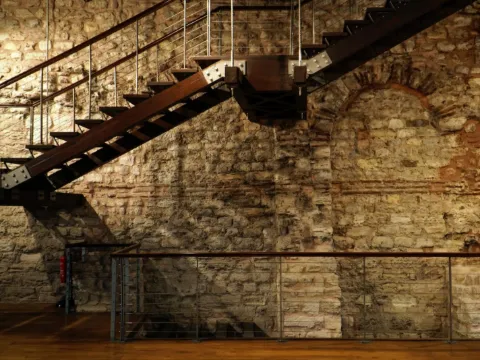 Escalier à limon d'acier boulonné soutenu par des tirants devant un mur de pierre ancienne