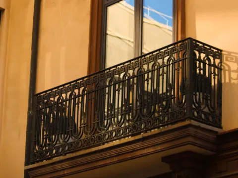Balcon en fer forgé noir à frise grecque devant une baie cintrée, lumière dorée