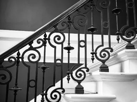 Balustres en fer forgé noir à volutes et fuseaux le long d'un escalier blanc, vue en noir et blanc