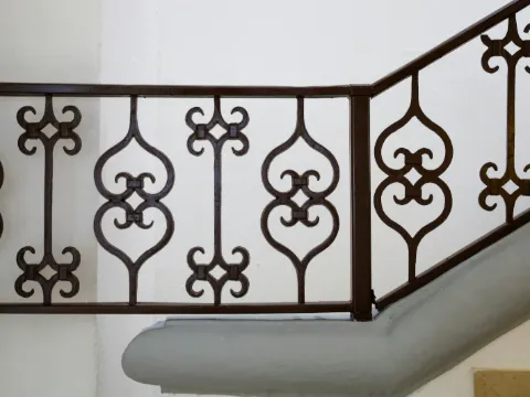 Rampe d'escalier en fer forgé brun à motifs d'ogives et de fleurons dans une cage d'escalier blanche