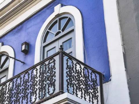 Garde-corps de porte-fenêtre en fer forgé noir à motifs floraux sur une façade bleu violet à baies cintrées