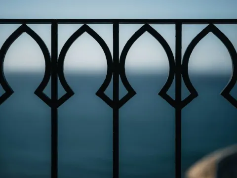 Garde-corps en acier noir à motifs d'arcatures et barreaux fins, devant la mer bleue