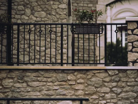 Garde-corps barreaudés en fer noir à fleurons sur des murs en pierre apparente