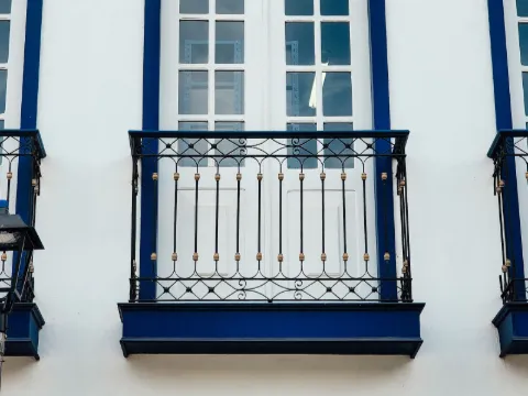 Porte-fenêtre blanche à encadrement bleu avec garde-corps en fer forgé noir sur façade lisse