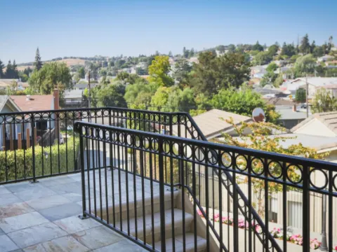 Terrasse carrelée avec garde-corps en fer noir à cercles et rampe d'escalier, vue sur les toits
