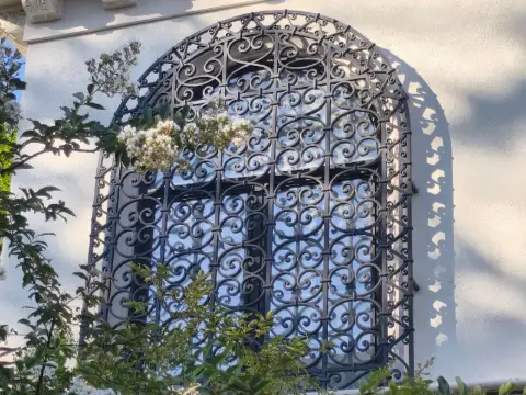 Fenêtre en arc d'une demeure blanche fermée par une grille de fer forgé très ouvragée