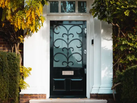 Porte d'entrée noire vitrée à décor de fer forgé, dans un portique blanc