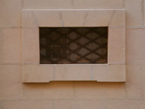 Ouverture rectangulaire d'un mur de pierre blonde fermée par une grille de fer croisillonnée