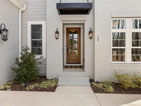 Auvent noir en acier suspendu au-dessus d'une porte vitrée en bois, façade en brique blanche et lanternes