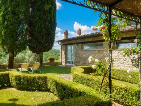 Angle d'une pergola en fer forgé noir et toit de roseaux au-dessus de rosiers, devant une maison en pierre
