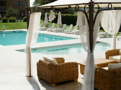 Pavillon en fer forgé sombre aux rideaux blancs, salon en osier au bord d'une piscine bordée de pelouse