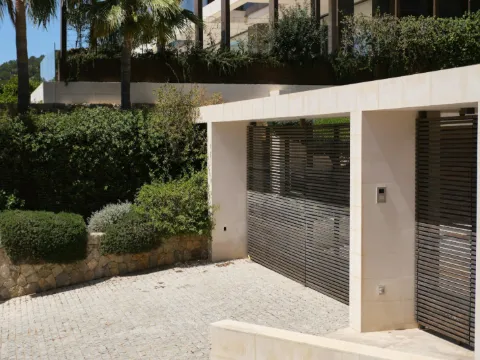 Portail coulissant à lames horizontales sombres dans un portique de pierre calcaire, jardin méditerranéen