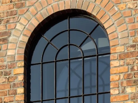 Fenêtre cintrée à fins carreaux d'acier noir dans un mur de briques ensoleillé