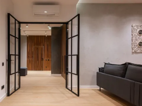 Porte vitrée à deux vantaux ouverts, carreaux d'acier noir, entre un salon et un couloir