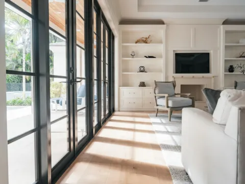 Salon clair avec portes-fenêtres à petits carreaux d'acier noir ouvertes sur la piscine